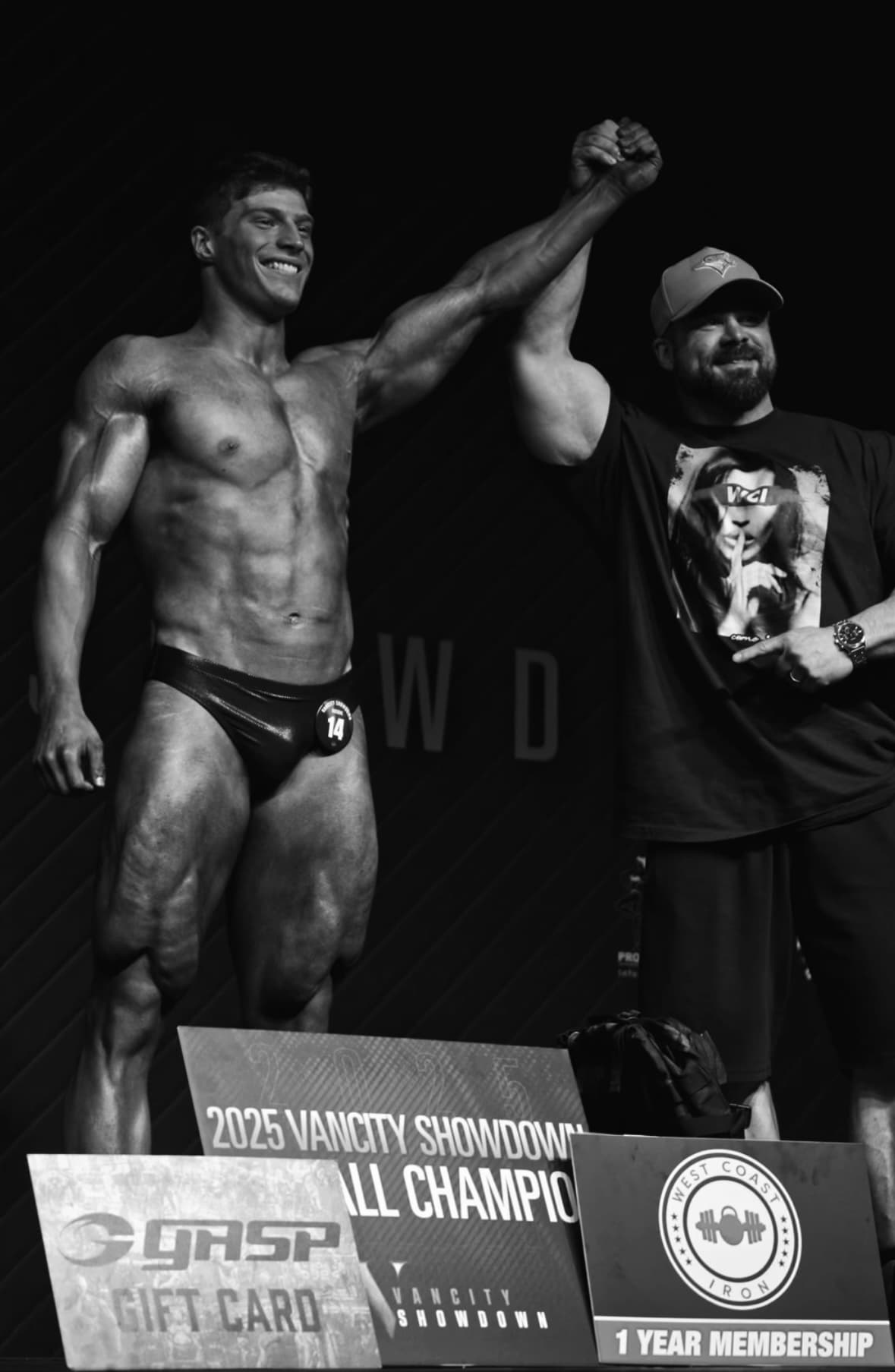 Smiling bodybuilder has his arm raised in victory at the 2025 Vancity Showdown competition.