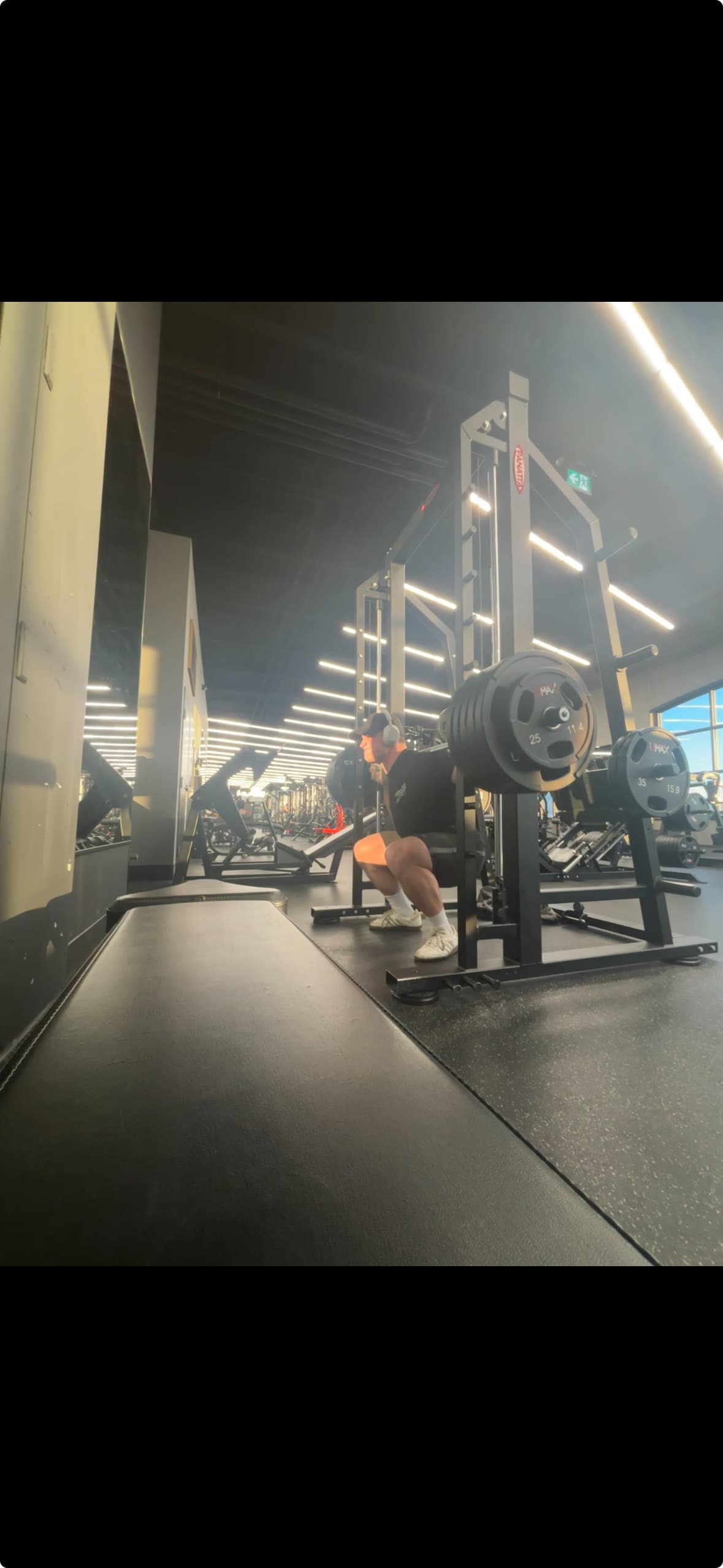 Man performing a deep barbell squat in a squat rack at a brightly lit gym.